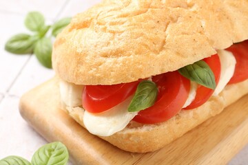 Tasty sandwich with mozzarella cheese, tomatoes and basil on light tiled table, closeup