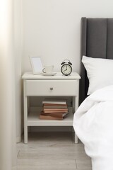 Bedside table with alarm clock, coffee and frame near bed indoors
