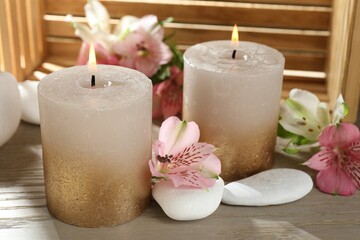 Burning candles, stones and lily flowers on wooden table, closeup