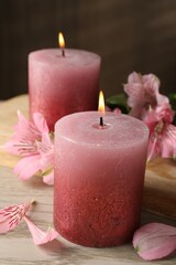 Burning candles and lily flowers on white wooden table, closeup