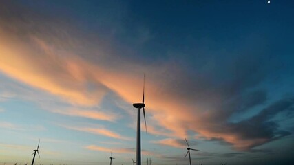 Wind turbines stand tall against a vibrant sunset sky