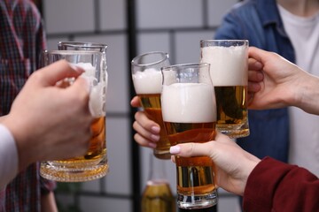 Friends clinking glasses of beer indoors, closeup