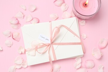 Stack of letters with phrase I Love You, burning candle and petals on pink background, flat lay