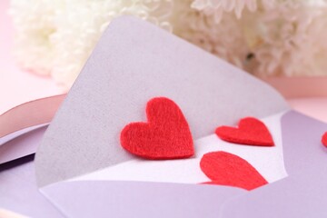 Love letter. Envelope, red hearts, ribbon and flowers on blurred background, closeup