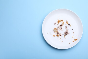 Dirty plate with crumbs and cream on light blue background, top view. Space for text