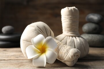 Herbal bags, spa stones and plumeria flower on wooden table, closeup