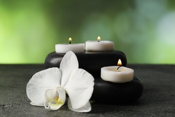 Spa stones, burning candles and orchid flower on grey table, closeup