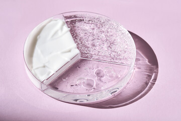 A three-section petri dish with textures of cream, cosmetic oil and serum. Purple background.