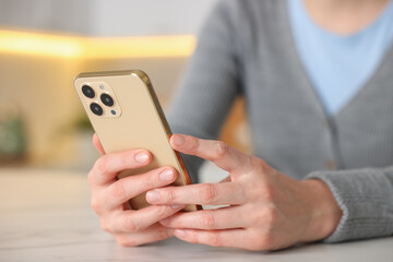 Woman using smartphone at table indoors, closeup