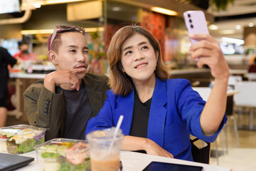 Gender diverse coworker business team eating salad and working digitally taking selfie with phone