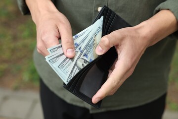 Man putting money into wallet outdoors, closeup
