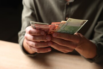 Man counting money at wooden table, closeup