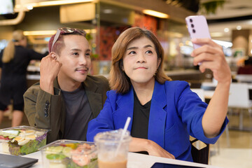 Gender diverse coworker business team eating salad and working digitally taking selfie with phone