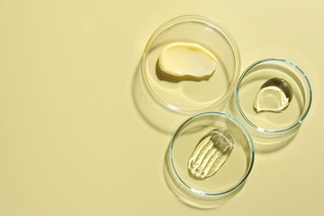 Different cosmetic products in Petri dishes on pale yellow background, flat lay. Space for text