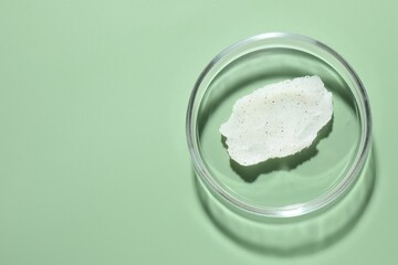 Cosmetic product in Petri dish on green background, top view. Space for text