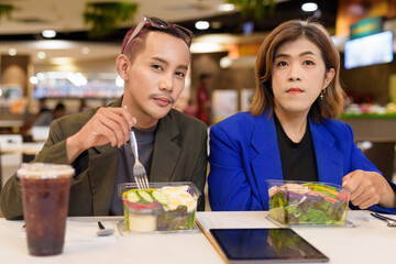 Gender diverse coworker business team eating salad and working digitally