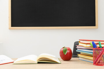 Different stationery and red apple on wooden table near blackboard indoors