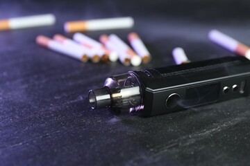 Electronic smoking device and cigarettes on black table, closeup