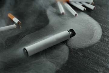 Electronic smoking device and cigarettes on black table, closeup