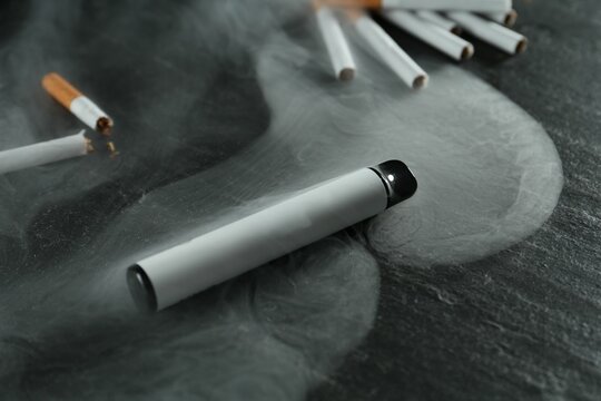 Electronic smoking device and cigarettes on black table, closeup - Powered by Adobe