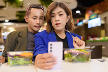 Gender diverse coworker business team eating salad and working digitally taking selfie with phone
