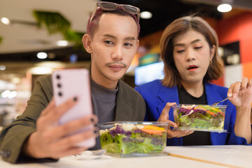 Gender diverse coworker business team eating salad and working digitally taking selfie with phone