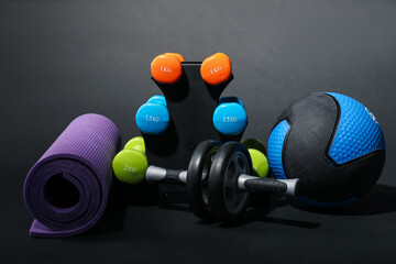 Medicine ball, dumbbells, fitness mat and ab wheel on black background