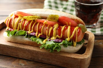 Tasty hot dog and soda drink on wooden table, closeup