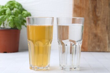 Glasses with clean and dirty water on white tiled table, closeup