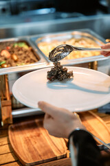 Serving delicious black risotto from buffet tray with spoon in a buffet restaurant setting