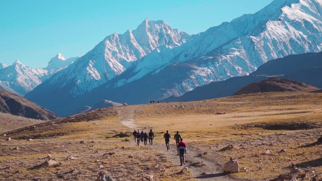 Rear view shot of group of people walking towards the snowy Himalayan mountain peak near Chandratal Lake in Spiti Valley, Himachal Pradesh, India. Group of hikers walking in front of the Himalayas.