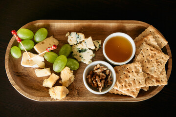 Gourmet cheese platter with grapes, crackers, honey and walnuts on wooden tray