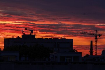 Fototapeta premium Dramatic Sunset in Red-Violet and Pink Over City Skyline with Construction Crane.
