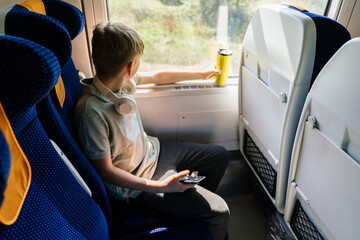 Teenager holding thermos and smartphone by train window