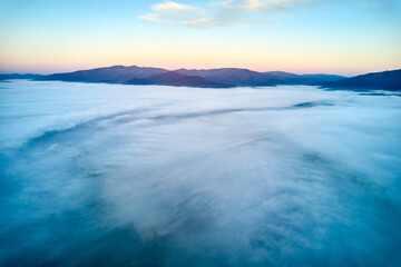 Breathtaking aerial view at dawn, showcasing vast sea of clouds enveloping mountain landscape. Subtle hues of rising sun paint sky in soft pastels, creating tranquil and ethereal scene.