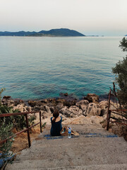 a beautiful girl sits on the stairs looking at the sea