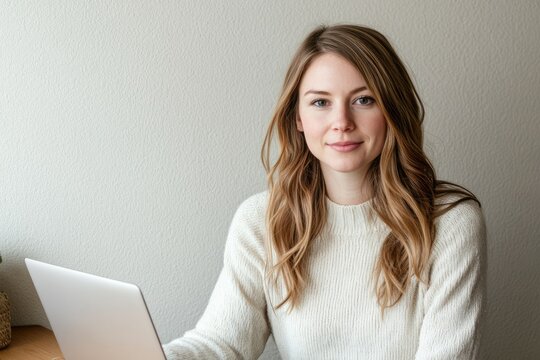A young woman with long brown hair smiles gently while working on her laptop.