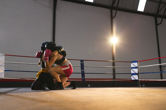 Female opponents grappling in boxing ring with headgear, gloves between colored ropes, copy space