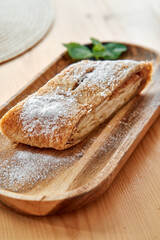 Delicious apple strudel on wooden plate with powdered sugar dessert