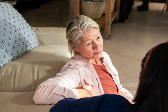 Female friends talking on beige couch in living room holding light-blue cushion near wicker baskets