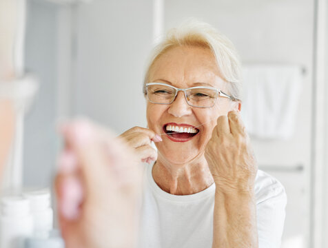 Portrait of an elderly senior woman is cleaning brushing his teeth using dental floss in front of mirror in bathroom. Dental hygiene, vitality and beauty concepts