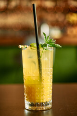 Refreshing yellow citrus cocktail with black straw and mint garnish on brown table
