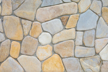 This natural stone wall presents a chaotic yet harmonious appearance. Varied sizes and shapes of beige and gray stone pieces create an interesting texture, ideal for backgrounds or construction projec