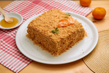 Napoleon cake with tangerine garnish on white plate and red checkered cloth