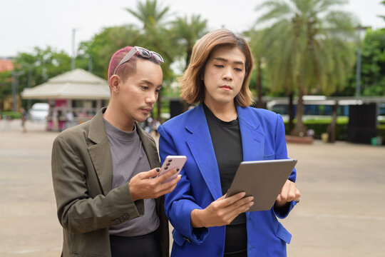 Gender diverse business coworker professionals using technology on city street - Powered by Adobe