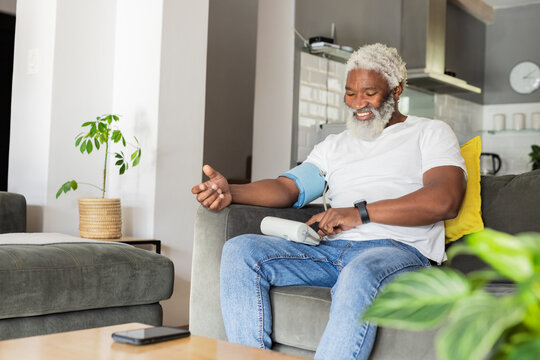 Senior African American man using blood pressure monitor while sitting on sofa at home, copy space