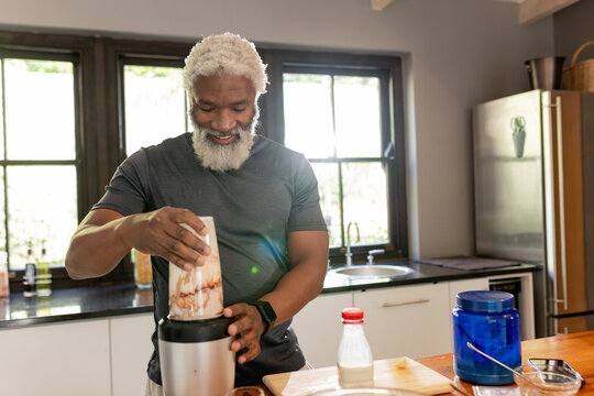 Senior African American man wearing athletic shirt blending smoothie at kitchen island with blender - Powered by Adobe