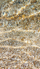 Pebbles and seashell fragments under clear shallow water with sunlight reflections. Natural underwater texture. Summer beach background. Seashore and marine life concept. Top view texture background.
