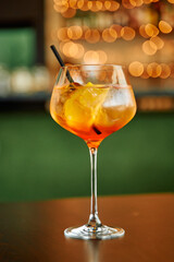Elegant aperol spritz with ice cubes on bar table amidst warm bokeh lights