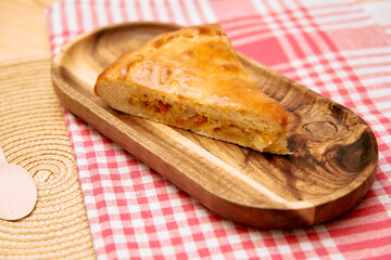 Appetizing slice of baked empanada pastry on rustic wooden plate with red checkered cloth
